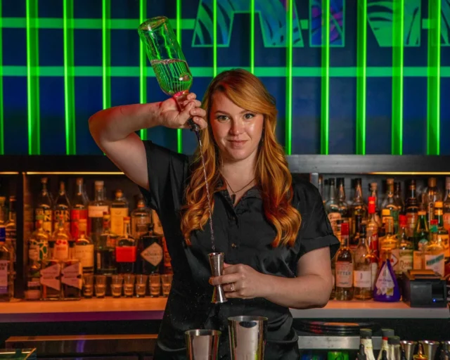 bartender Mara pours high while looking into camera